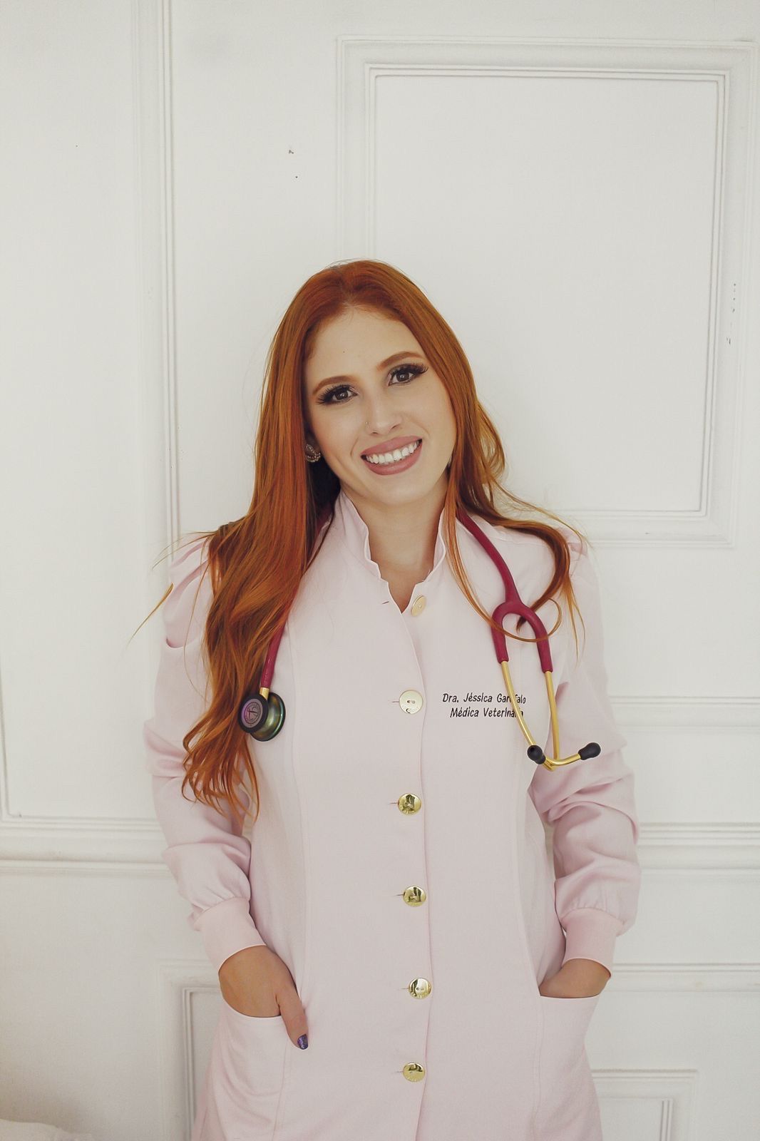 Dra. Jéssica Garofalo, de jaleco rosa e estetoscópio, sorrindo em retrato profissional.
